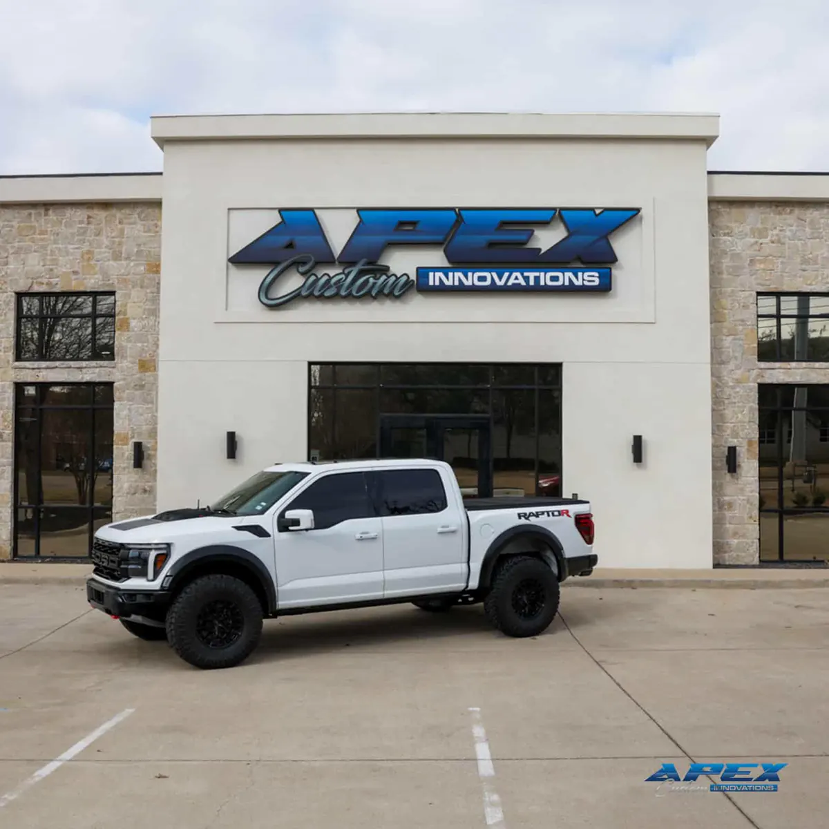 White 2025 Ford F-150 Raptor R in front of the Apex Custom Innovations storefront